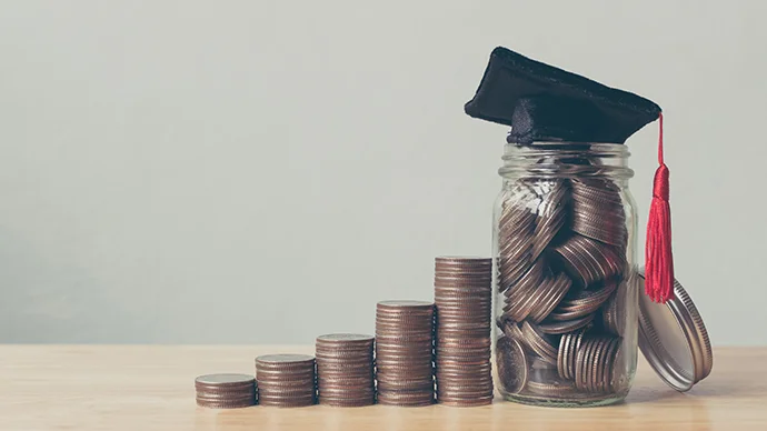 Increasing stack of coins next to a filled coin jar with a graduation cap