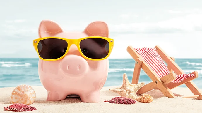 3 Tips to Keep Your Summer Vacation Within Budget Piggy bank wearing shades while at the beach